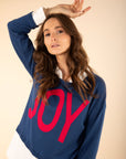 Woman wearing a blue sweater with 'JOY' in red letters against a beige background