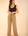 Woman wearing a black tank top and beige wide-leg pants on a beige background