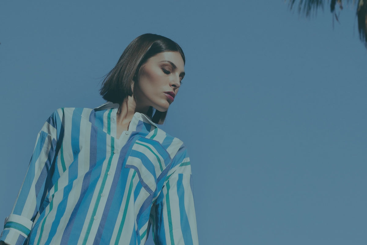 Model in a blue and white striped shirt and denim against a terracotta wall
