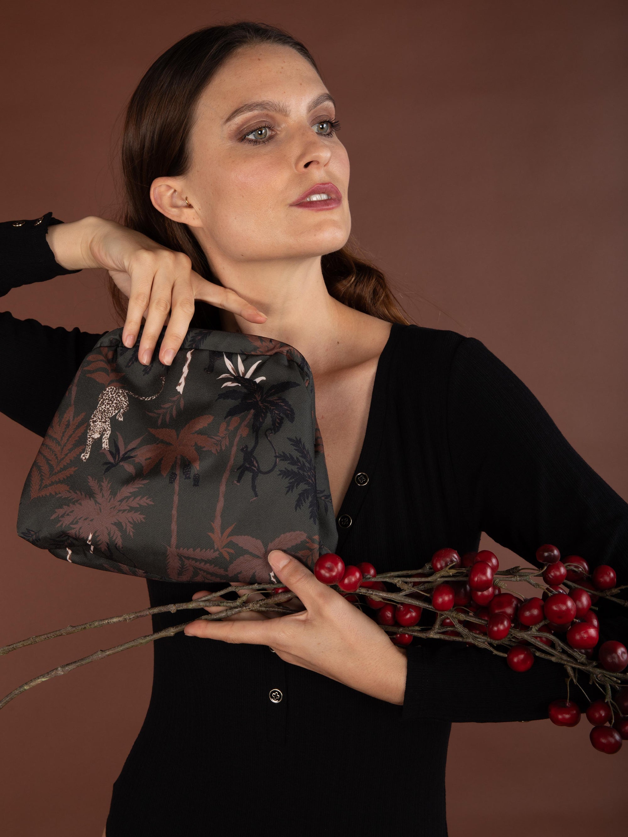 Woman holding a black embroidered clutch with red berries on a brown background