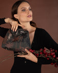 Woman holding a black embroidered clutch with red berries on a brown background