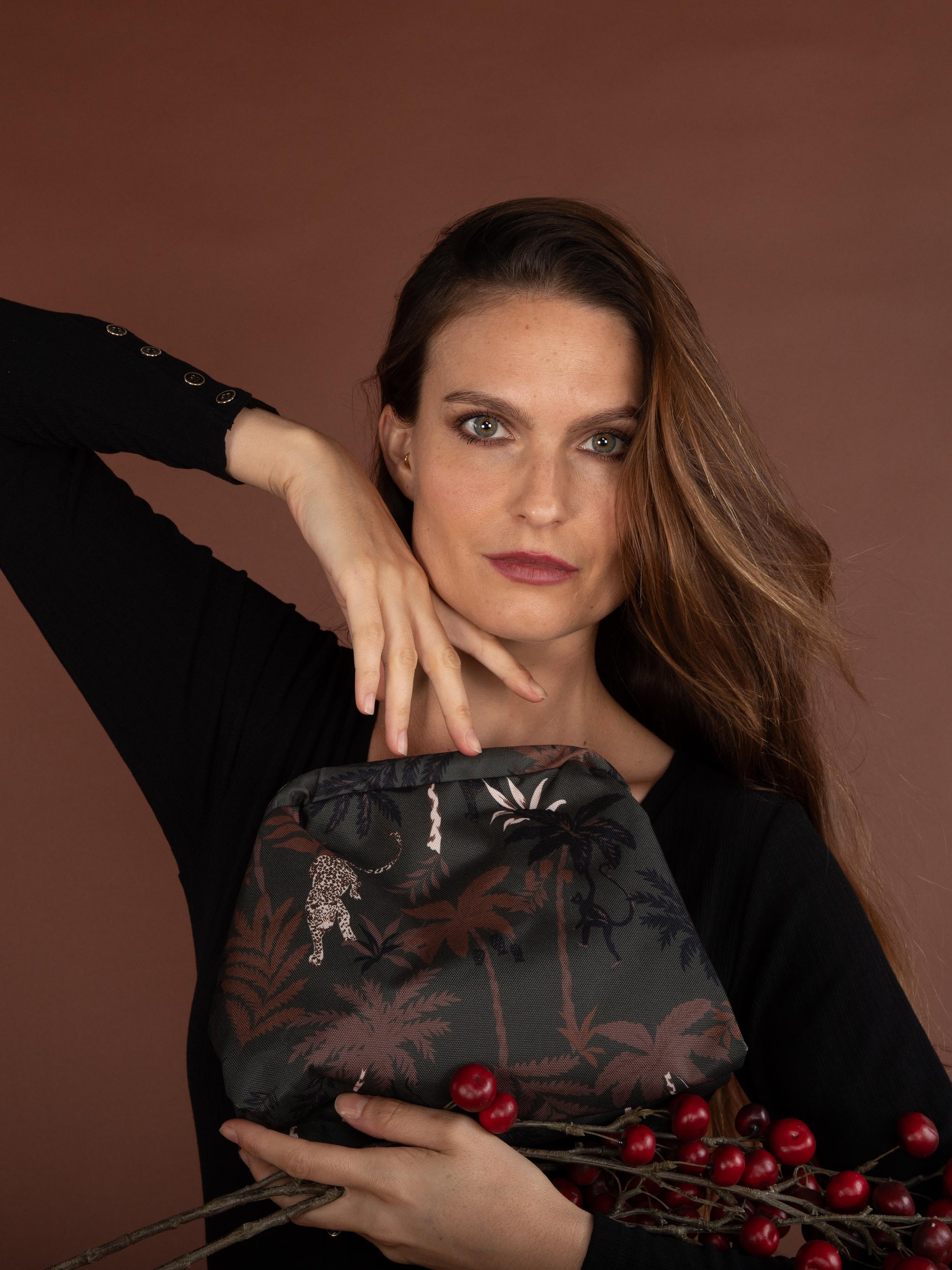 Woman holding a dark pouch with palm tree design against a brown background